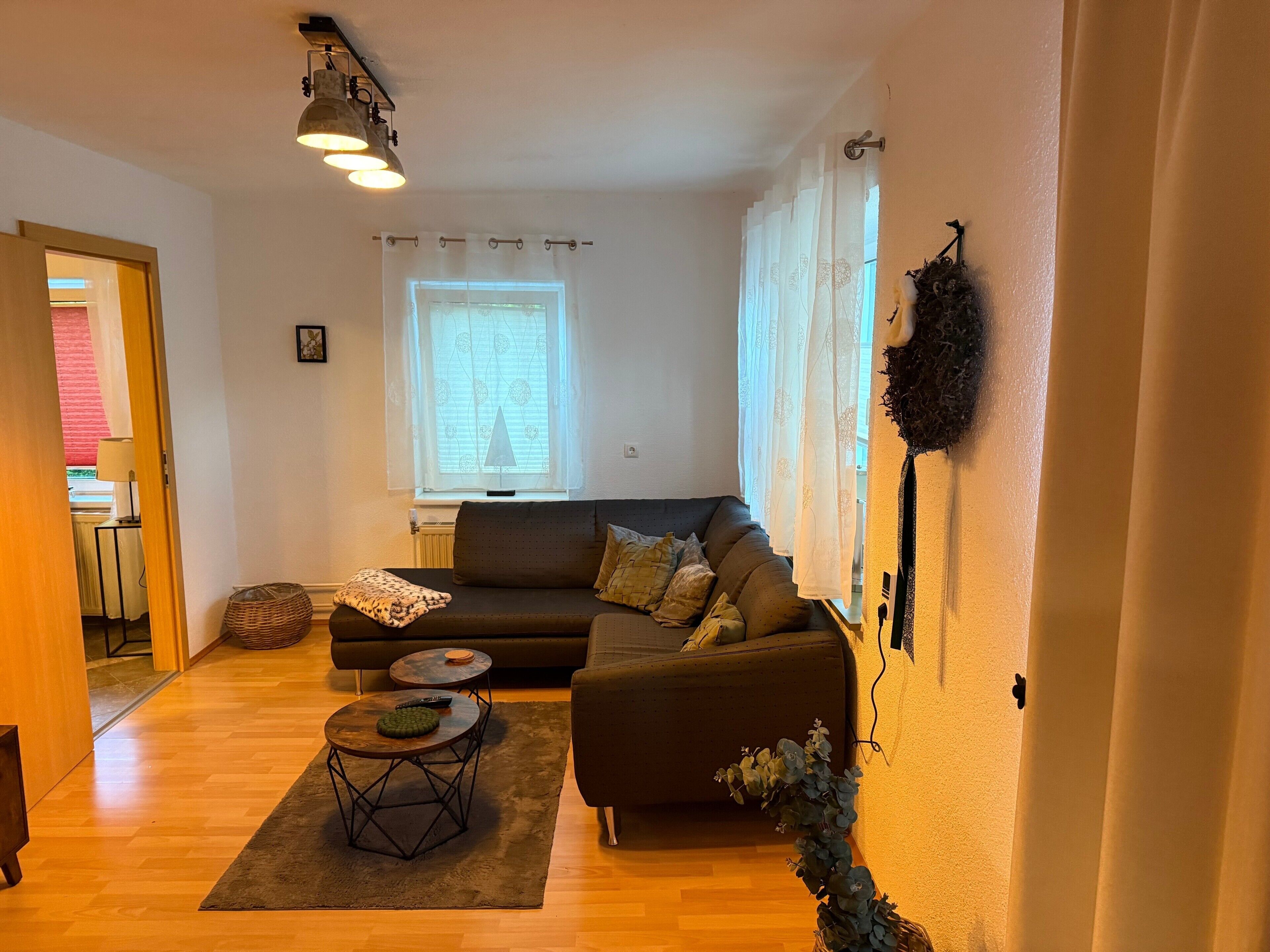 Ein Wohnzimmer mit einer Couch, einem runden Couchtisch, einer Lampe und einem Fenster mit Vorhängen.