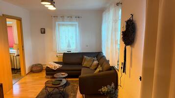 Ein Wohnzimmer mit einer Couch, einem runden Couchtisch, einer Lampe und einem Fenster mit Vorhängen.