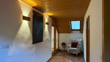 A hallway with a wooden ceiling, a patterned chair, a wall-mounted picture, and a small window.