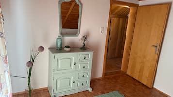 A room with a light green dresser, a mirror, a vase with flowers, and a wooden door.