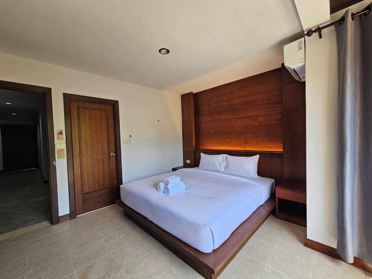 Una habitación de hotel con una cama, cabecera de madera, una ventana con cortinas y una puerta.