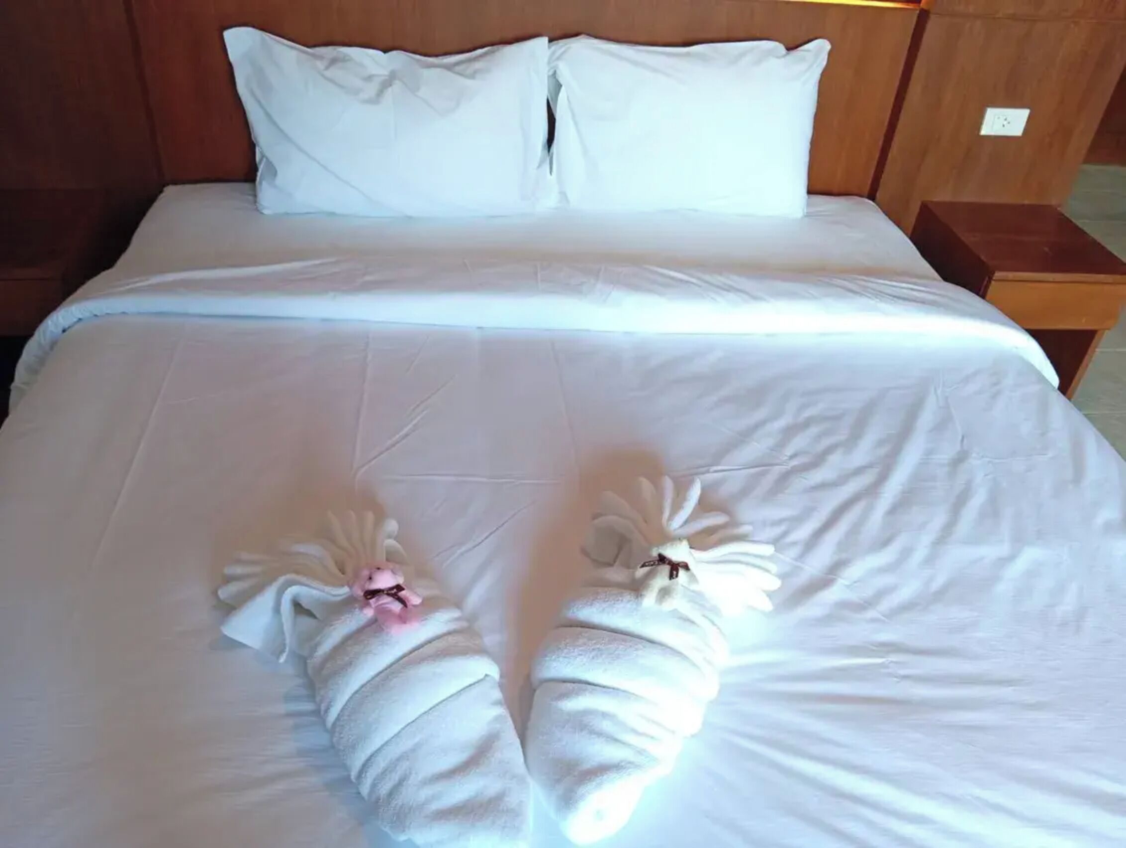 Una cama con ropa blanca y dos toallas dispuestas sobre ella.