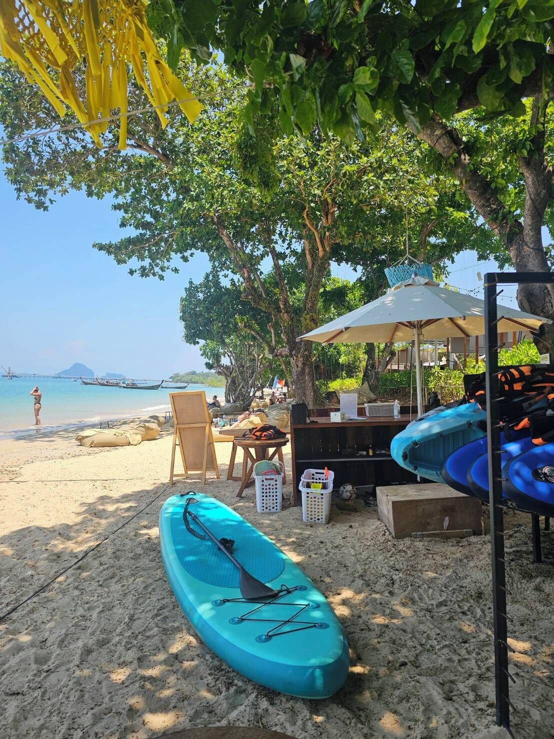 Un paisaje de playa con un kayak, una mesa con sillas y una sombrilla.