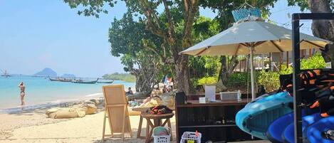 Um cenário de praia com um caiaque, uma mesa com cadeiras e um guarda-sol.