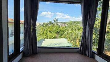 Una habitación con un ventanal, cortinas y vistas a zonas verdes y edificios.
