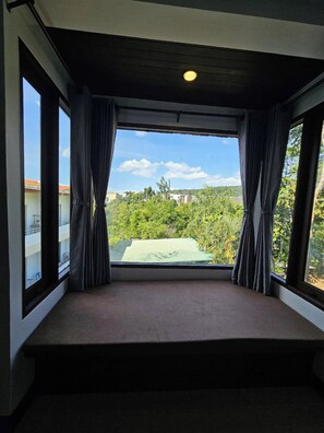 A room with a large window, curtains, and a view of greenery and buildings. - Anda See House (Krabi)