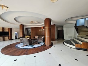 A lobby with a central seating area, a staircase, and a wall with the name 'ANDA SE'. - Anda See House (Krabi)