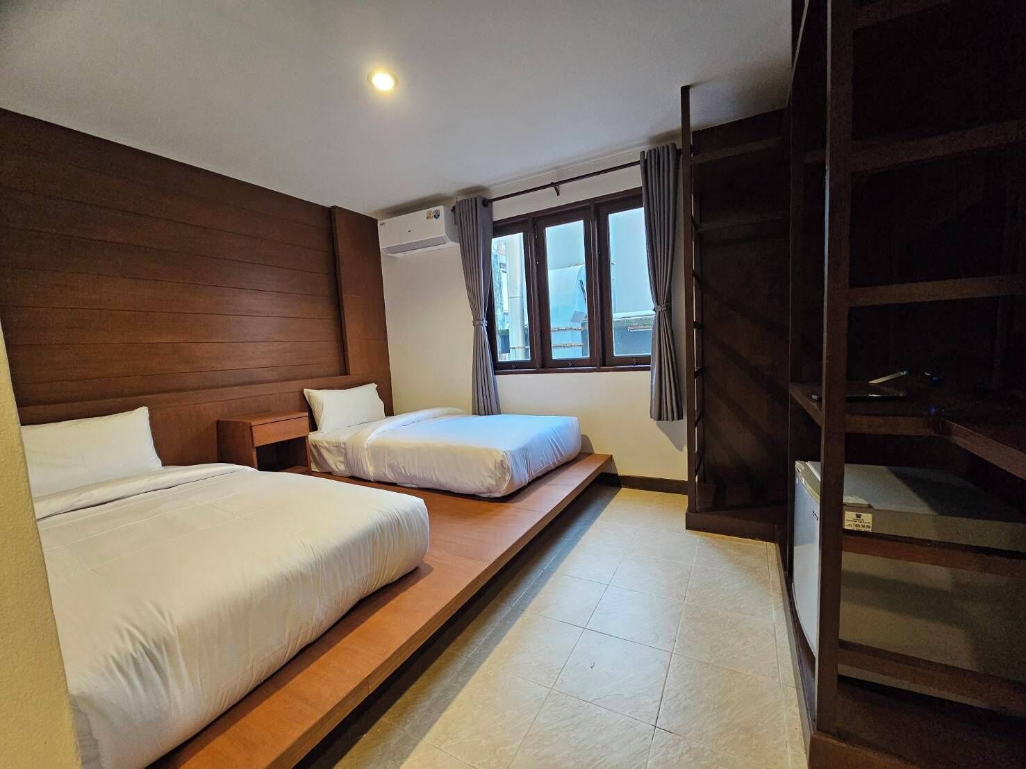 Ein Hotelzimmer mit zwei Betten, einem fensterbelaubten Fenster, einem Holz-Kopfteil und einem eingebauten Kleiderschrank.