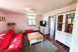 A living room with a red sofa, a wooden coffee table, a television, and a cabinet with glass doors.