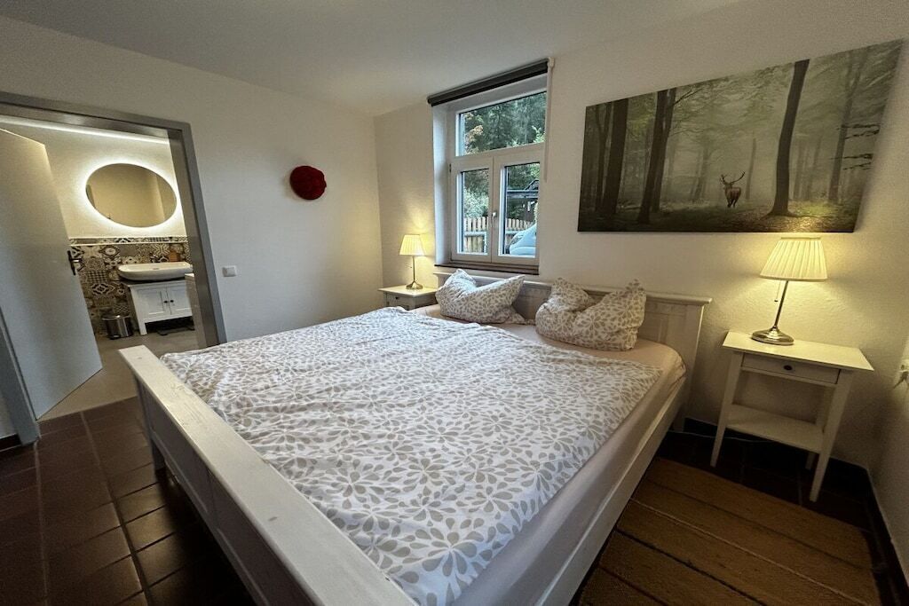 Ein Schlafzimmer mit einem Bett, einem Fenster, einem Bild und einem durch eine offene Tür einsehbarer Badezimmer.