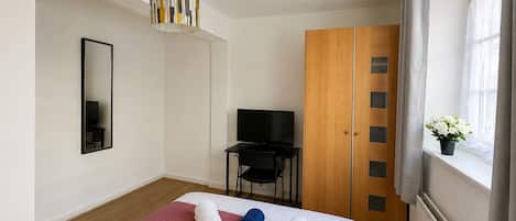 Une chambre d’hôtel avec un lit, une télévision, une armoire et une fenêtre avec des rideaux.