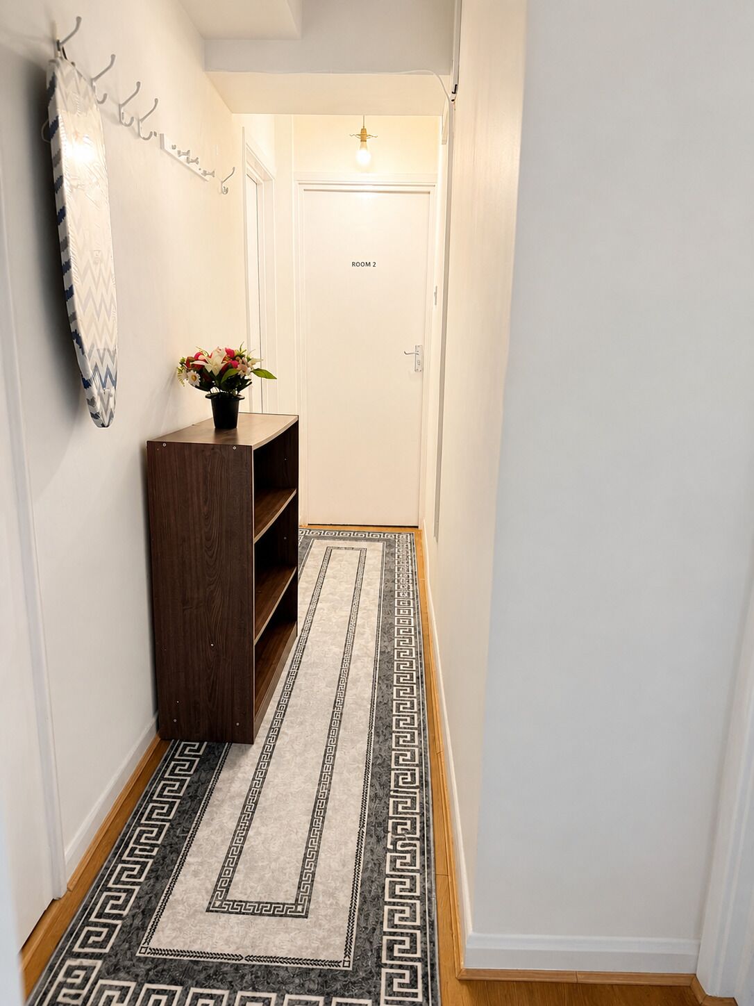 A hallway with a wooden bench, a patterned rug, and a door labeled 'ROOM 2'.