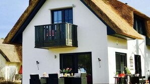 Una casa moderna de dos pisos con techo de paja, un balcón y un comedor con mobiliario exterior.