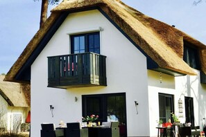 A modern two-story house with a thatched roof, a balcony, and a dining area with outdoor furniture. - My Little Zanzibar 2 (Zirchow)