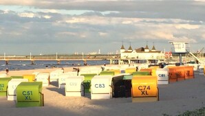 Ein Strand mit Reihen von nummerierten Strandhäusern, einem Rettungsturm und einem in der Ferne liegenden Gebäude mit mehreren Türmen.