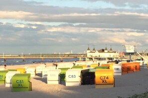 Ein Strand mit Reihen von nummerierten Strandhäusern, einem Rettungsturm und einem in der Ferne liegenden Gebäude mit mehreren Türmen.