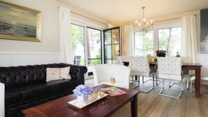 Ein Wohnzimmer mit einer schwarzen Ledersofa, einem Holztisch und einem weißen Sessel. Es gibt einen Essbereich mit Tisch und Stühlen, und eine Kristallleuchter hängt von der Decke.