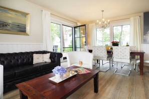 Ein Wohnzimmer mit einer schwarzen Ledersofa, einem Holztisch und einem weißen Sessel. Es gibt einen Essbereich mit Tisch und Stühlen, und eine Kristallleuchter hängt von der Decke.