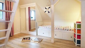 Kinderzimmer mit Hochbett, Kommode, einer Leiter und einem Regal mit Aufbewahrungsboxen.