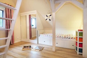 Kinderzimmer mit Hochbett, Kommode, einer Leiter und einem Regal mit Aufbewahrungsboxen.
