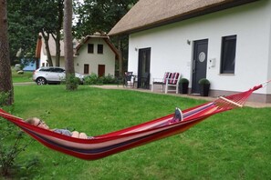 A hammock in a grassy area with a building in the background. - My Little Zanzibar 1 (Zirchow)