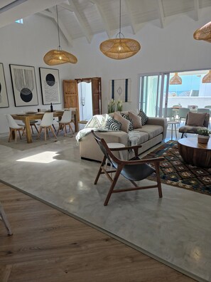 A spacious living area with a sofa, dining table, and chairs, a large window, and a ceiling with exposed beams.