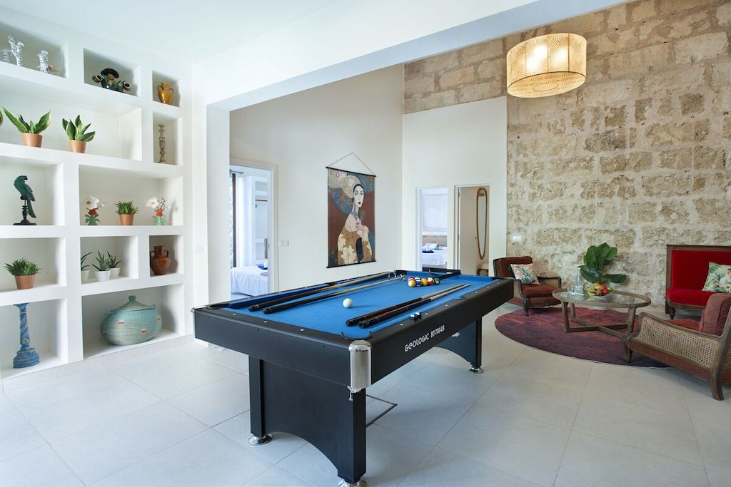 Een pooltafel in een ruimte met witte planken, een rode bank en een stenen muur.