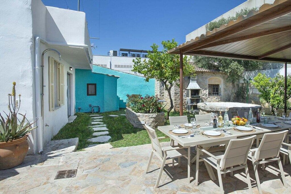 A patio with a table set for dining, surrounded by stone flooring and a small garden area with a blue wall and greenery.