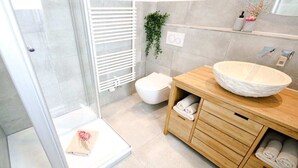 A modern bathroom with a glass shower enclosure, a wooden vanity with a large basin, and a toilet. - Holiday apartment with 2 bedrooms (Warnemünde)