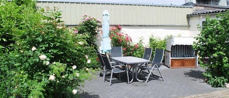 An outdoor patio area with a table and chairs, surrounded by lush greenery and flowering plants.