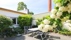 An outdoor patio area with a table and chairs, surrounded by lush greenery and white flowers. - Holiday apartment with 2 bedrooms (Warnemünde)