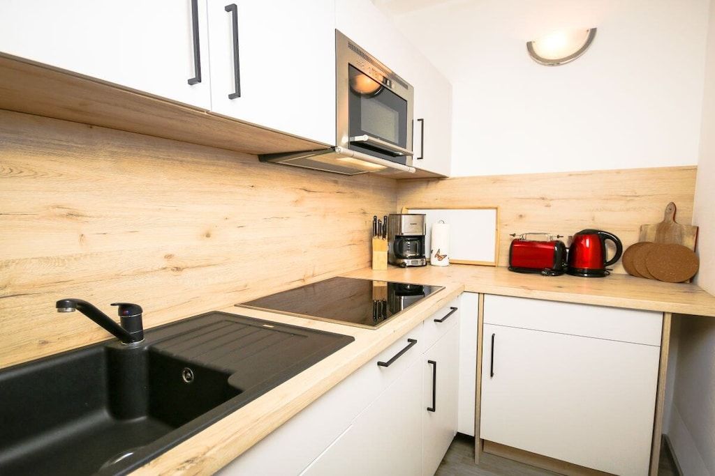 A modern kitchen with a black sink, white cabinets, a microwave, and a coffee maker.