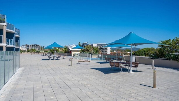 Une terrasse extérieure aménagée avec des sièges et des parasols, entourée d’immeubles.