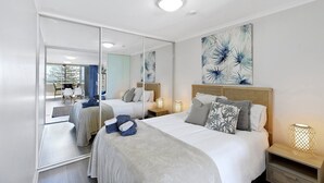 Une chambre à coucher moderne avec un grand lit, des tables de chevet, un miroir et des œuvres d’art accrochées au mur.