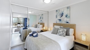 A modern bedroom with a large bed, bedside tables, a mirror, and artwork on the wall.