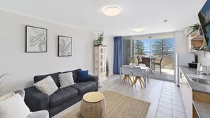 A modern living room with a sofa, a dining area with chairs, a kitchen with a sink, and a view of the outdoors. - NESUTO 408 - Waterview Apartment by HolidayCo. (Unknown)