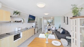 A modern kitchen with a dining area, a sofa, and a view of the outdoors.