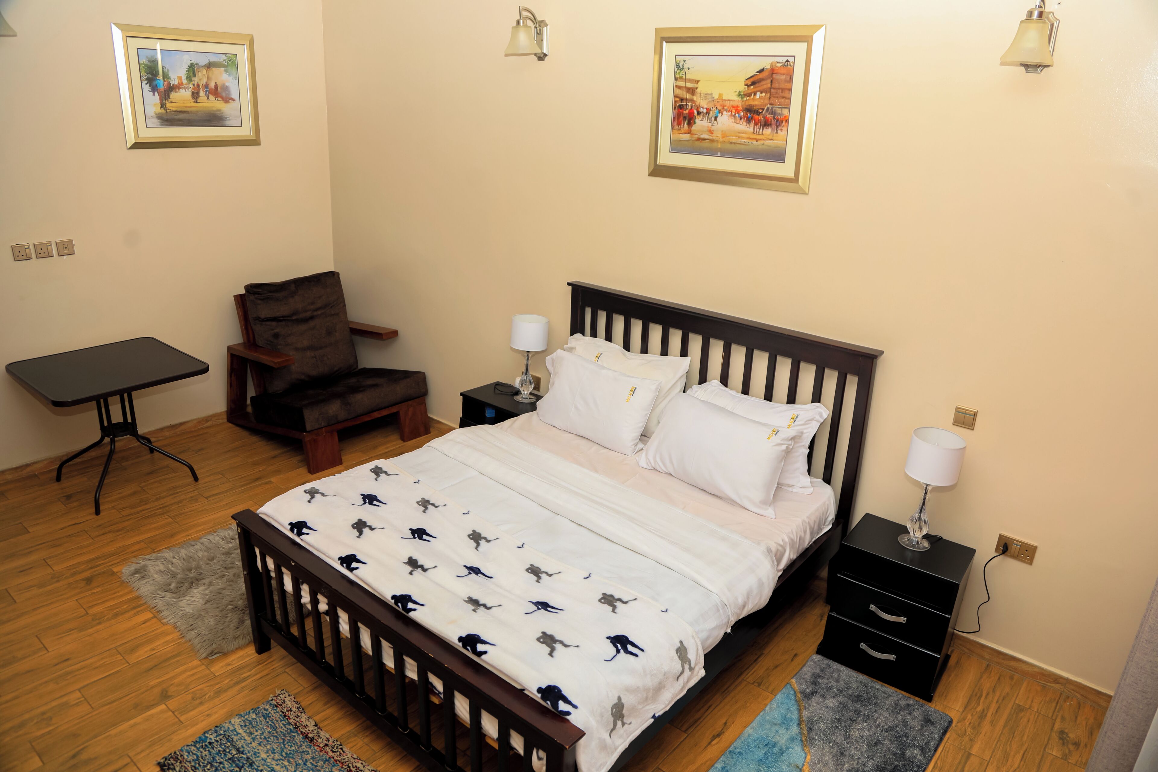 Een slaapkamer met een bed, een stoel, een tafel en twee schilderijen aan de muur.