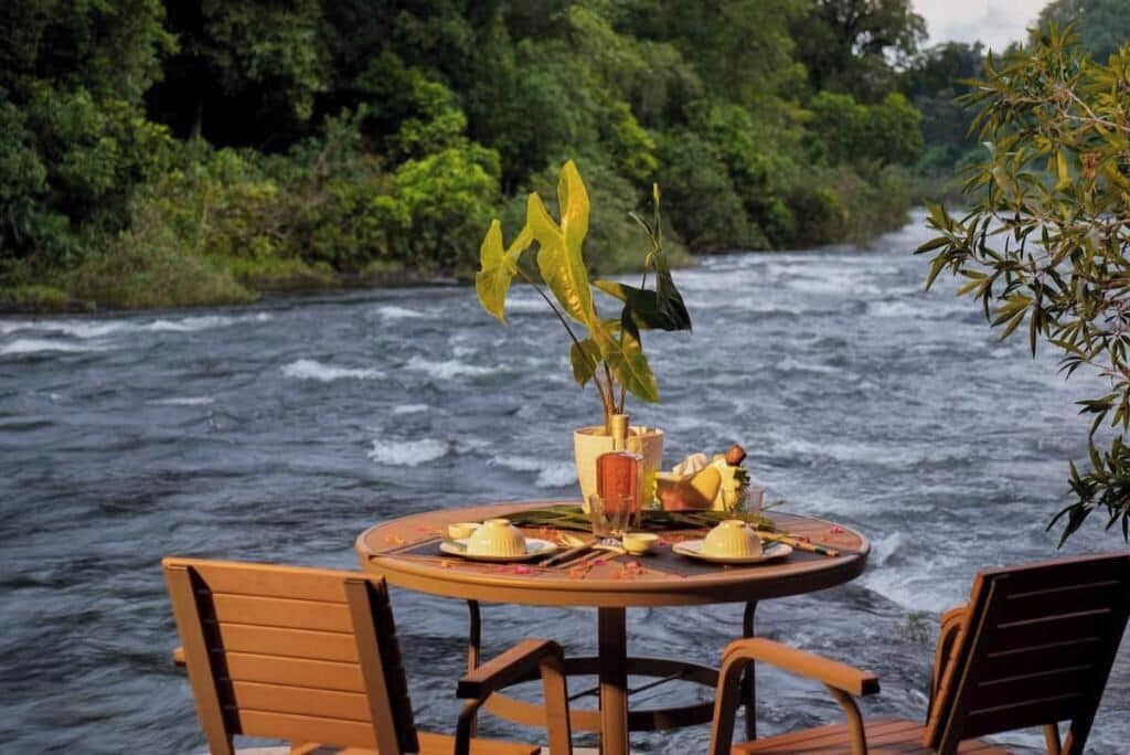 A round table with chairs set up by a river, with a plant in a vase on the table.