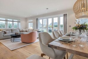 A spacious living area with a sofa, coffee table, and dining table set for a meal. - Bals Horsatal 15b / Rüm Hart (Wenningstedt)