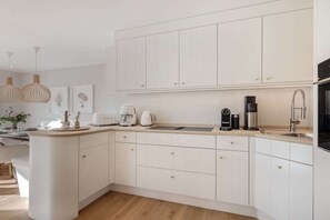 A modern kitchen with white cabinetry, a central island, and a built-in oven. - Bals Horsatal 15b / Rüm Hart (Wenningstedt)