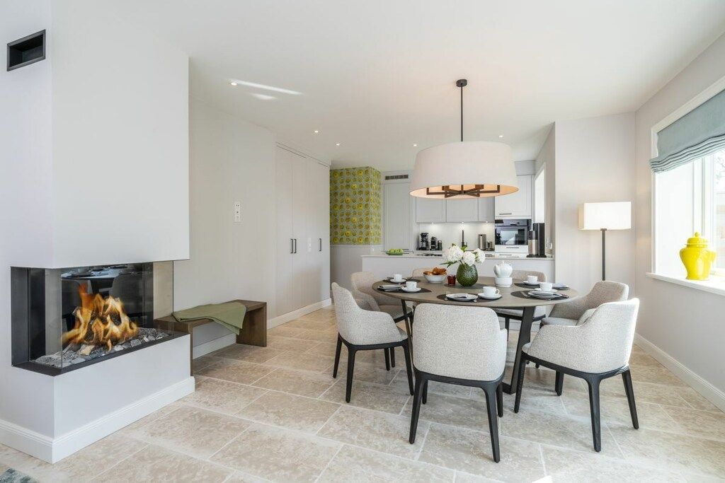 A modern dining area with a fireplace, a dining table with chairs, and a kitchen in the background.