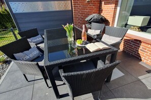 An outdoor patio with wicker furniture, a glass table, and a bottle of rosé wine. - Holiday apartment with 1 bedroom (Grömitz)