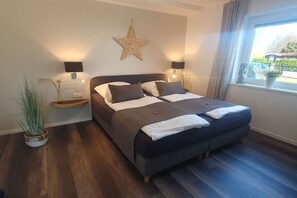 A bedroom with a large bed, bedside lamps, a star decoration, a window with a view, and a plant. - Holiday apartment with 1 bedroom (Grömitz)