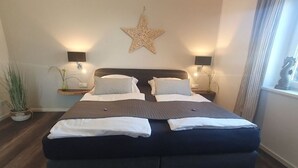 Un lit double avec une tête de lit sombre, deux tables de chevet avec des lampes, une décoration en forme d’étoile sur le mur et une plante en pot.