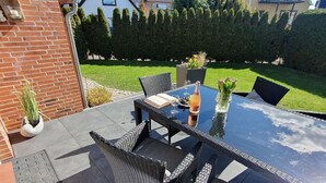 Une terrasse extérieure avec une table à plateau de verre, des chaises en osier et un pot de fleurs.