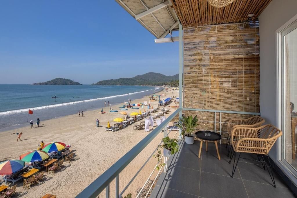 A balcony with wicker furniture overlooking a beach with umbrellas and lounge chairs.