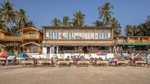 Un edificio frente a la playa con varios balcones, mobiliario exterior y palmeras al fondo.
