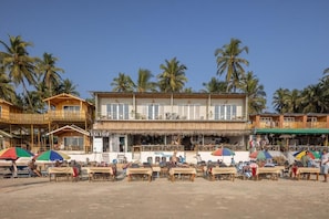 A beachfront building with multiple balconies, outdoor seating, and palm trees in the background. - Royal Touch Beach Huts (Canacona)
