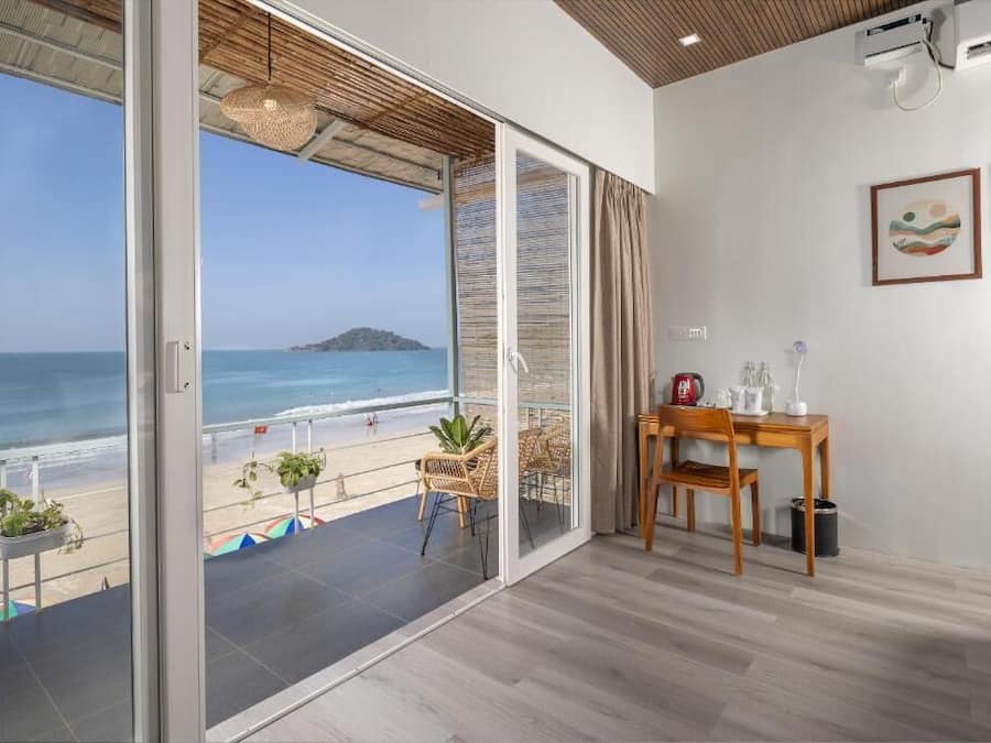 A room with a large sliding glass door leading to a balcony with a view of the beach and ocean.